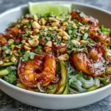 Stir-fried Asian Noodle Bowl topped with chopped peanuts and cilantro, served with lime wedges on the side.