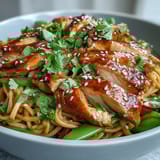 Hearty noodles tossed with chicken, carrots, and snap peas, garnished with sesame seeds and fresh cilantro. 