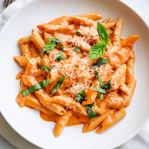 Penner pasta coated in a smooth roasted red pepper sauce, garnished with fresh basil and a sprinkle of Parmesan cheese.