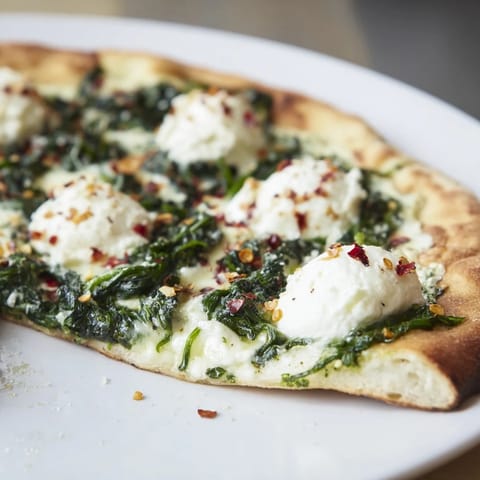 A freshly baked Spinach Ricotta Pizza slice being lifted, revealing melted mozzarella and fragrant garlic butter beneath vibrant green spinach.