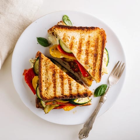 A close-up of golden, crusty Roasted Veggie Caprese Grilled Cheese, with melted mozzarella, roasted peppers, and fresh basil between the slices.