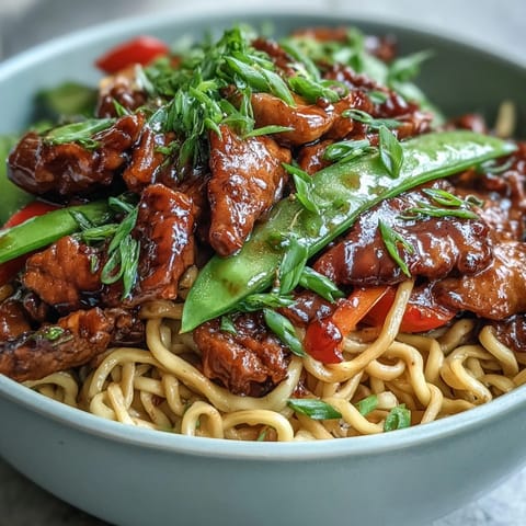 Tongs mixing cooked noodles and crisp vegetables into a hot wok, creating a steamy, savory Pork Noodle Stir-Fry.