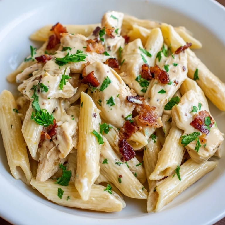 Golden slices of chicken and smoky bacon mingle with penne pasta in a luscious cream sauce, garnished with fresh parsley.