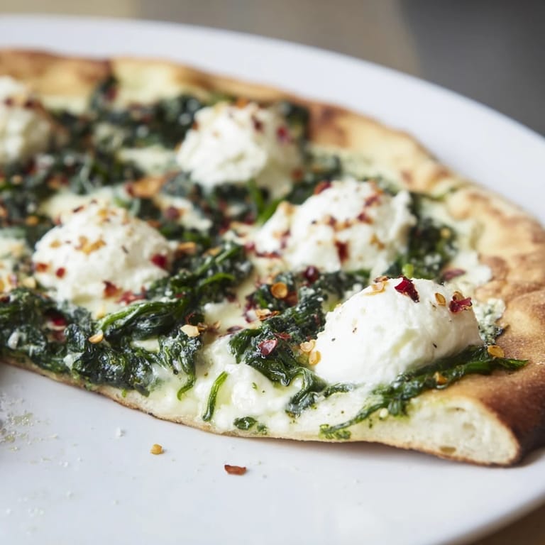 A freshly baked Spinach Ricotta Pizza slice being lifted, revealing melted mozzarella and fragrant garlic butter beneath vibrant green spinach.