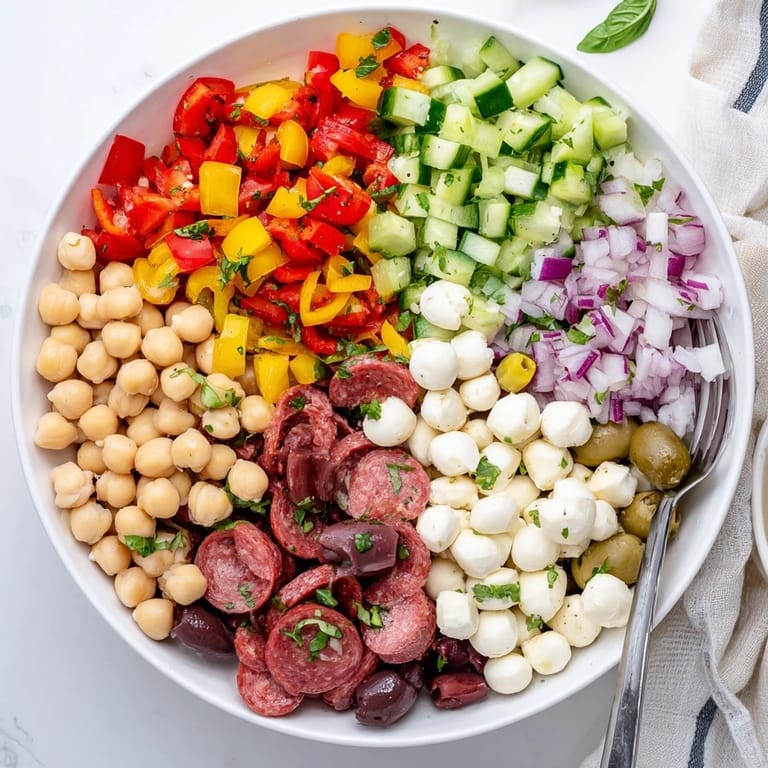 A vibrant bowl of crunchy antipasto chopped salad with mozzarella pearls and salami, ready to serve as a light Italian-American appetizer.