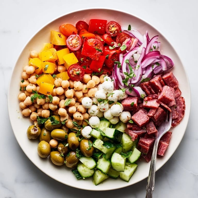 Freshly tossed crunchy antipasto chopped salad with diced cucumbers, bell peppers, olives, and herbs served in a white ceramic bowl.