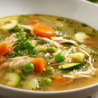 Steaming Spring Garden Chicken Soup with tender shredded chicken, peas, and bright parsley garnish on a rustic table.