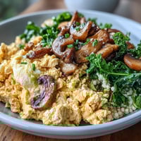 Golden scrambled tofu with sautéed mushrooms and kale over whole wheat couscous, garnished with fresh parsley.