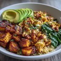 A colorful vegan breakfast bowl with savory tofu scramble, roasted sweet potatoes, quinoa, spinach, and avocado slices for a nourishing start.  